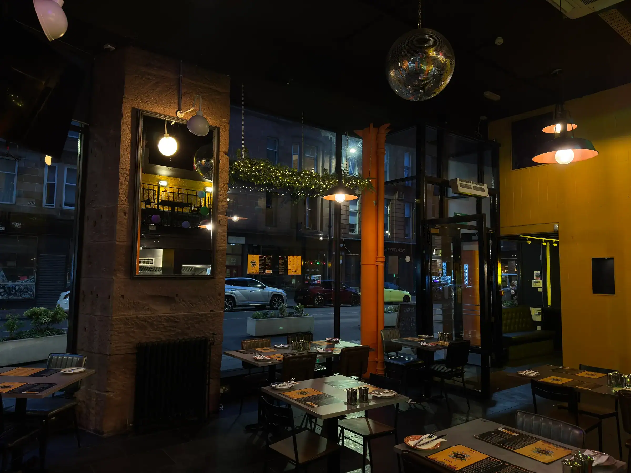 The dining room at Nukkad Café in the evening, with festoon lights and windows onto Bell Street, Merchant City, Glasgow